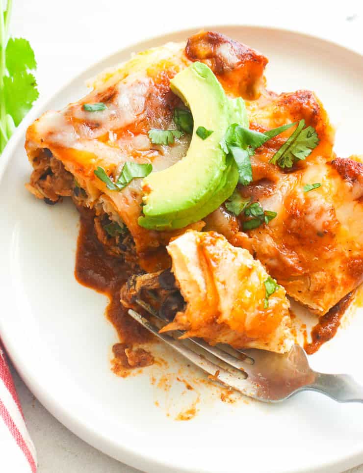Diving into a plate of homemade Mexican comfort food (tortillas, chicken, and chili sauce) topped with avocado.