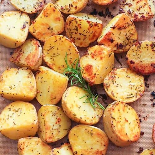 Pulling a baking sheet out of the oven loaded with rosemary roasted potatoes.
