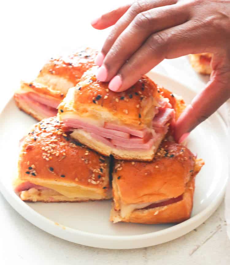 Ham and Cheese Sliders on a white plate with Imma taking one