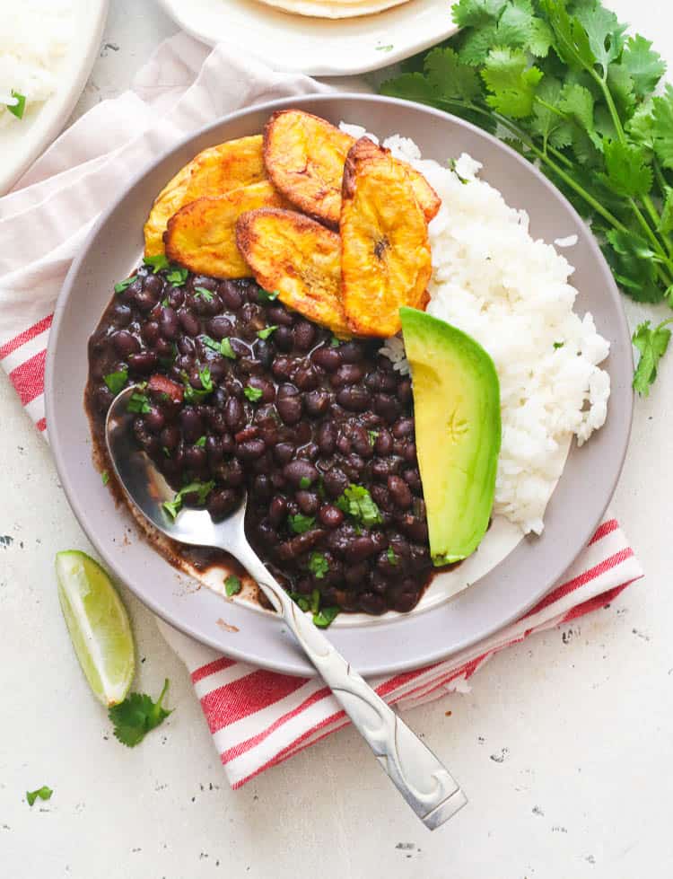 A meal with beans stew, rice, air fried plantains, and an avocado slice