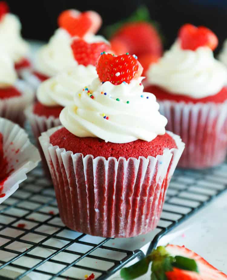 a batch of red velvet cupcakes with whipped cream and strawberry toppings