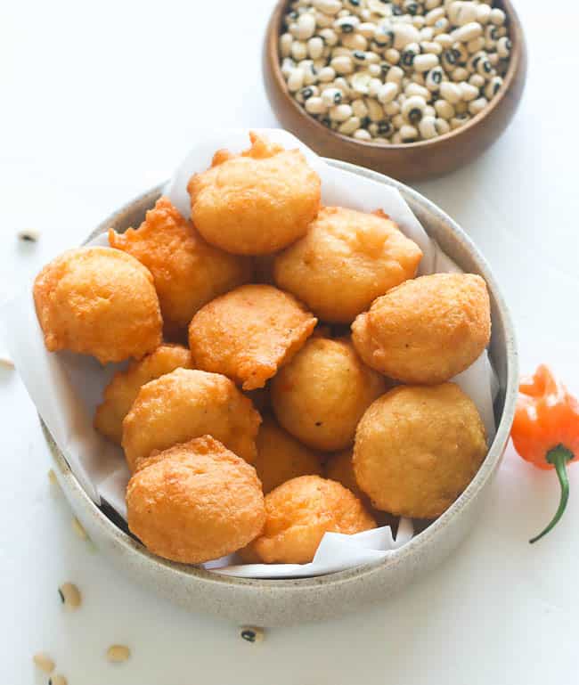 A Bowl of Black eyed Peas Fritters with Raw Black-Eyed Peas and Scotch Bonnet Pepper in the Background