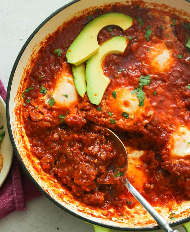 A pan of Eggs in Purgatory topped with avocado