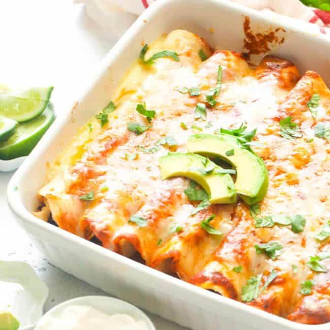 chicken enchiladas on a white baking this with slices of avocado on top