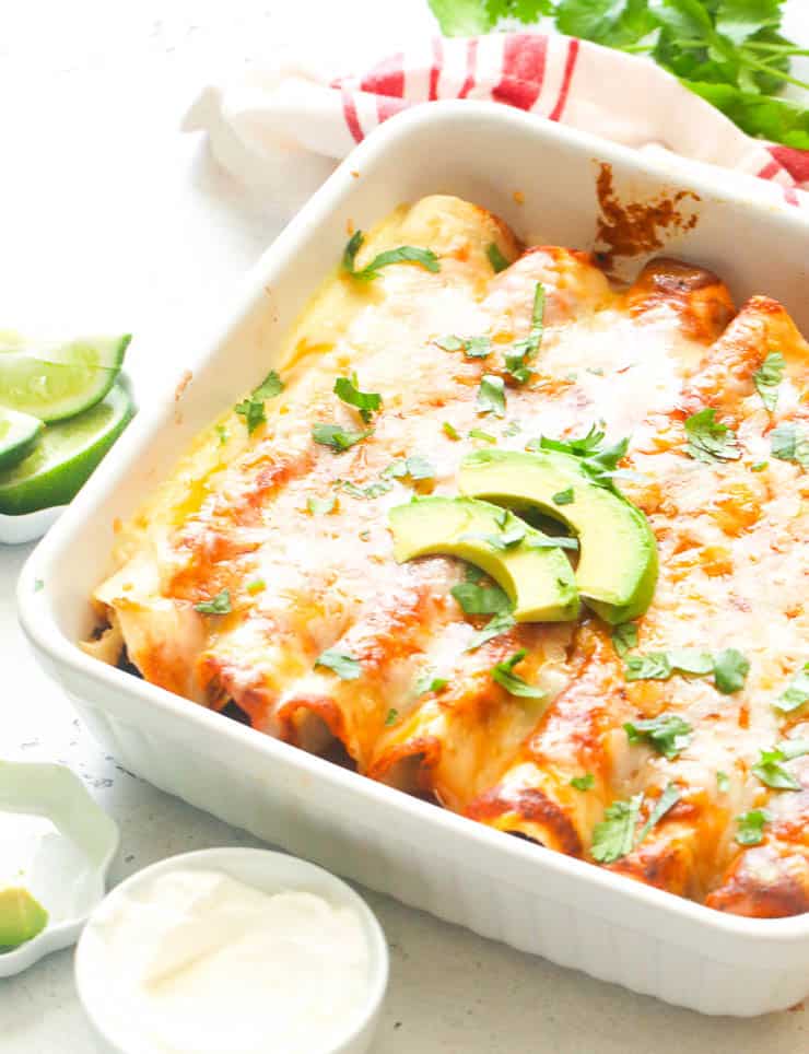 chicken enchiladas on a white baking this with slices of avocado on top
