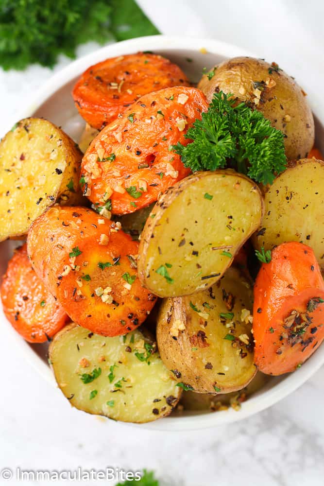 A bowl of Roasted Potatoes and Carrots topped with veggies