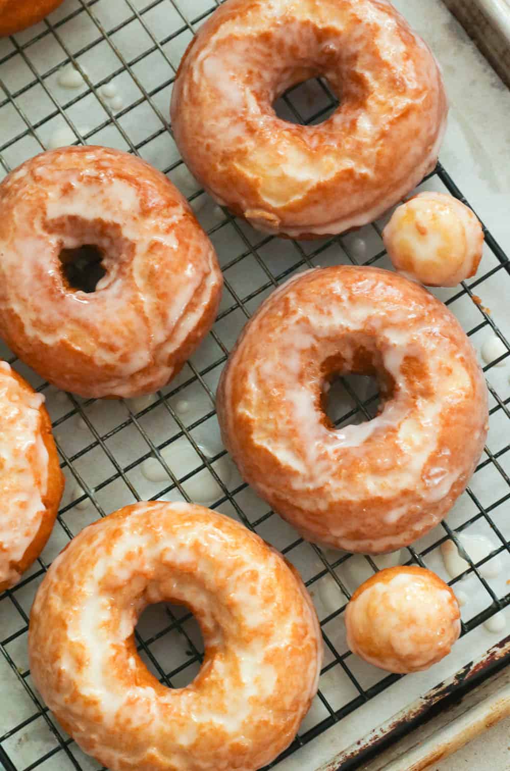 Sugar glazed doughnuts and holes lined on a cooling rack