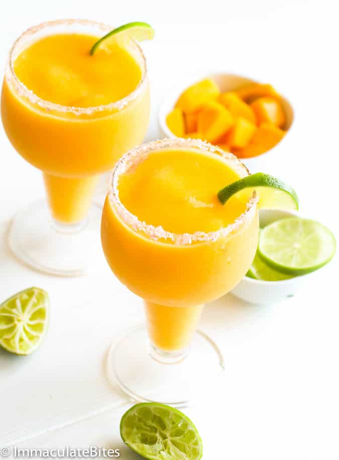 Two Frozen Mango Margaritas with slices of lime in the background