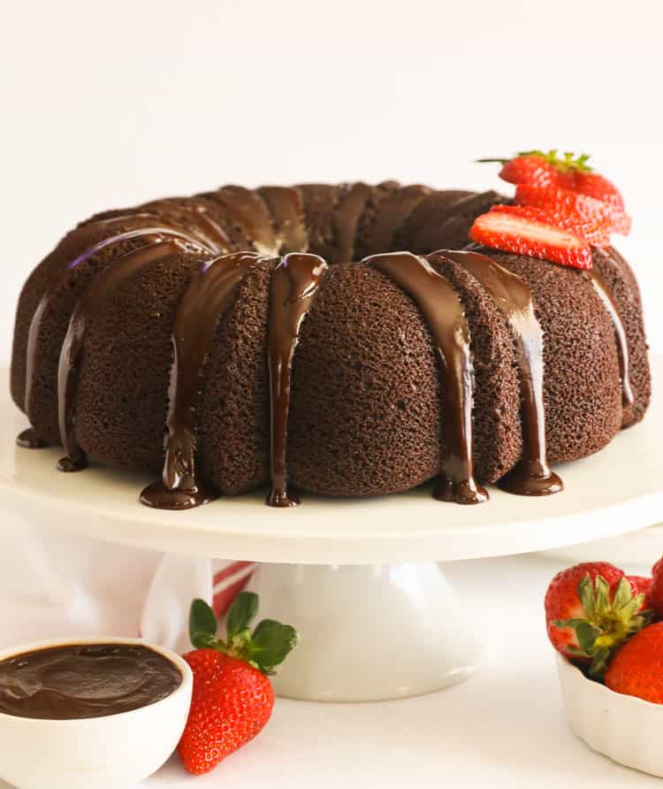 chocolate pound cake on a white cake stand with sliced strawberries on top