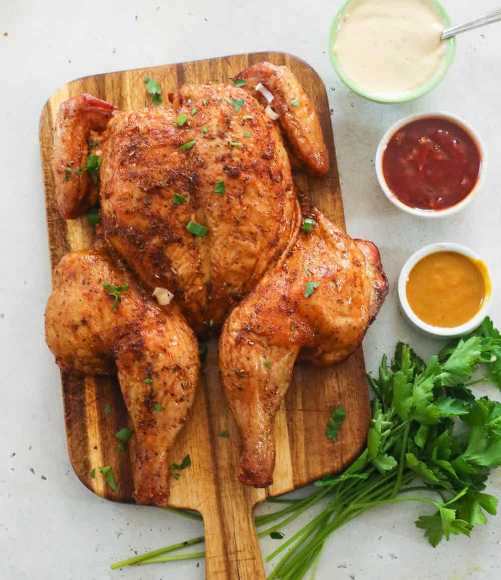 Whole spatchcock chicken on a board with sauces and parsley