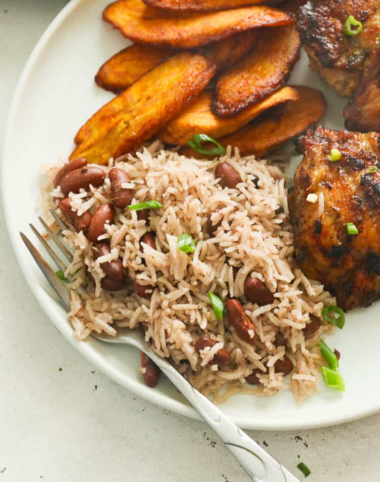 Jamaican rice and peas served on a white plate with chicken and fried plantains