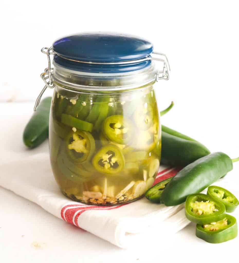Pickled jalapenos in a jar with jalapeno peppers scattered around the jar