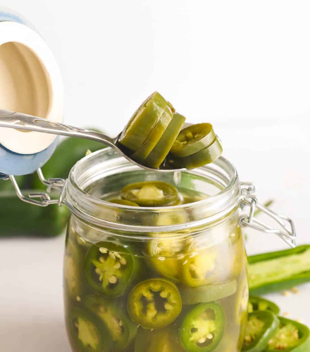 Slices of sliced jalapeno peppers on a spoon and in a jar