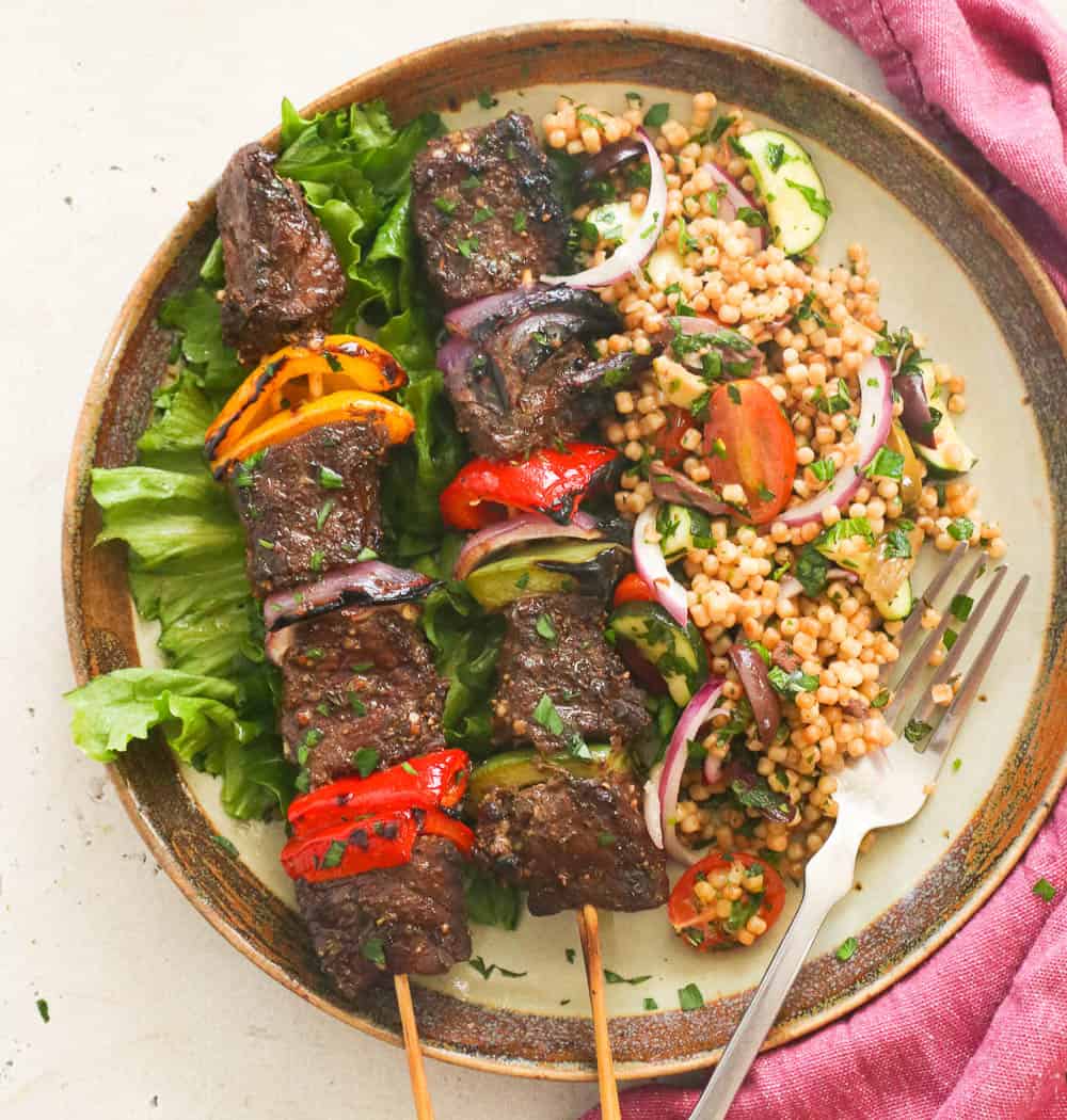 A plate with cous cous and steak kabobs