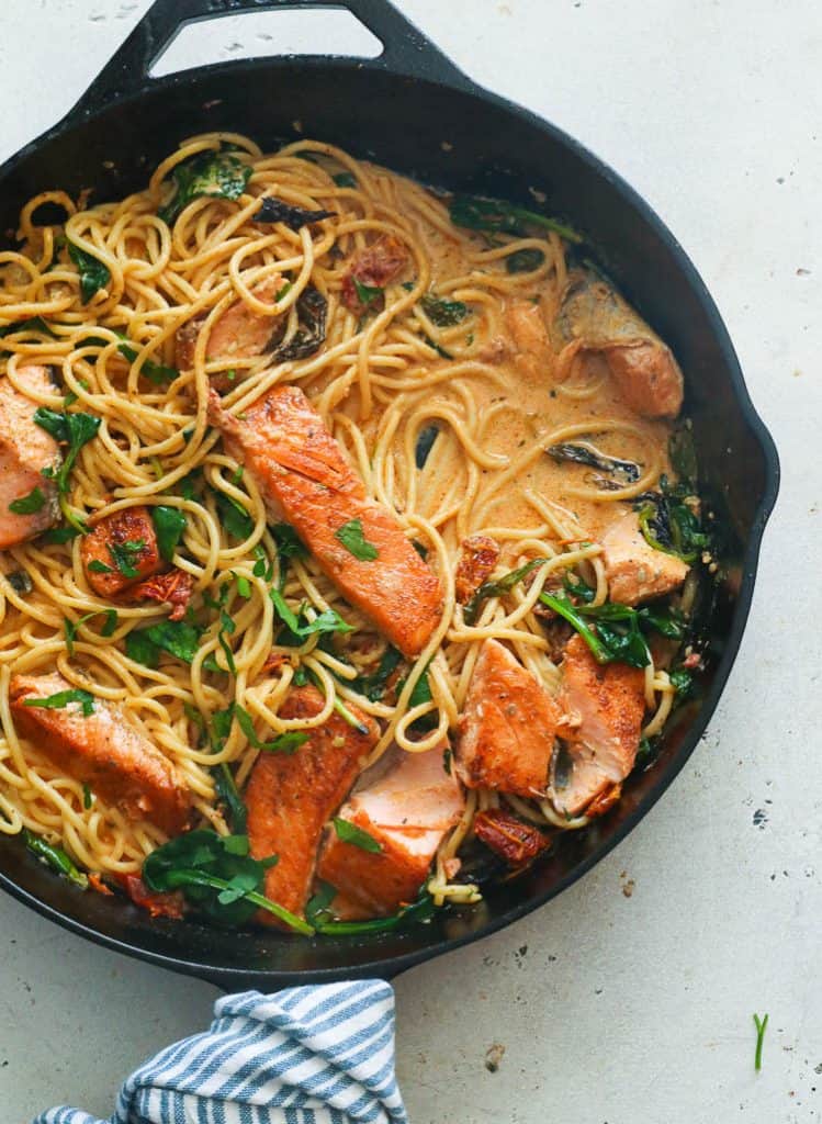 a skillet of pasta with salmon fillets and spinach