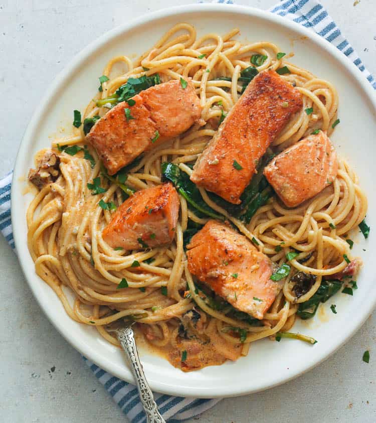 Creamy salmon pasta topped with salmon fillets on a white plate