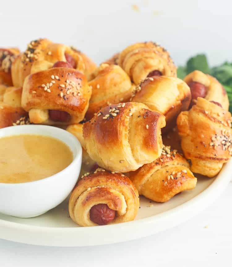 Ridiculously delicious Pigs in a Blanket with honey mustard on a white plate