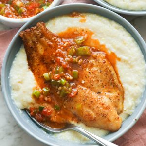 Fried fish with sauce on a bowl of gritz