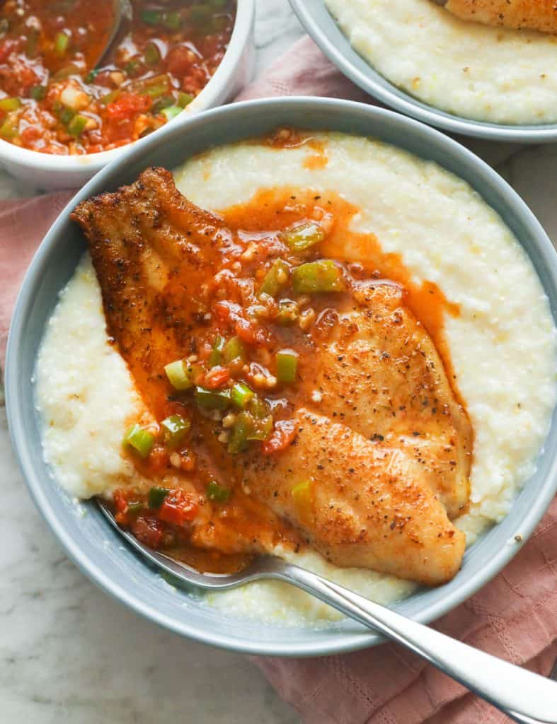 a bowl of grits with fried fish for toppings