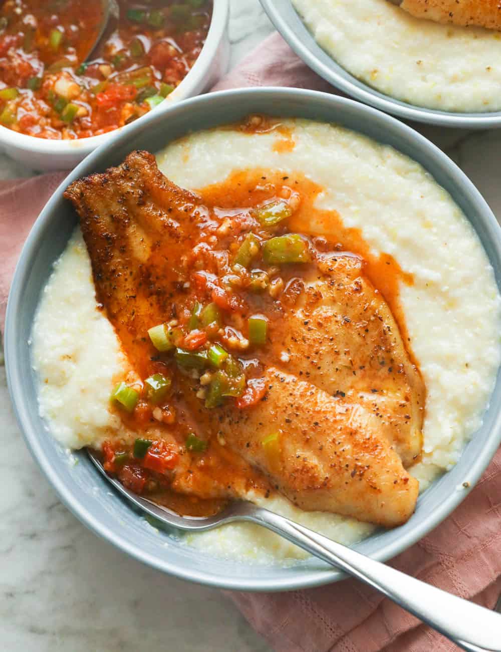 Fried fish with sauce on a bowl of gritz