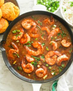 Shrimp gumbo in a black saucepan with cornbread on the side