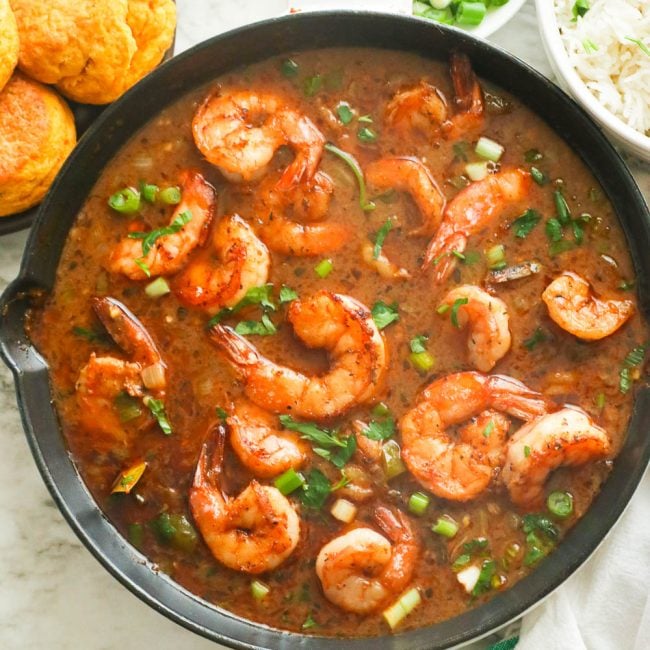 Shrimp gumbo in a black saucepan with cornbread on the side