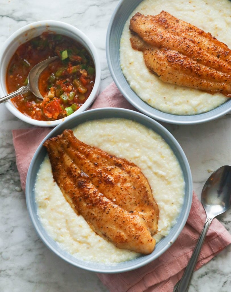 Two bowls of fish and grits served with sauce on the side