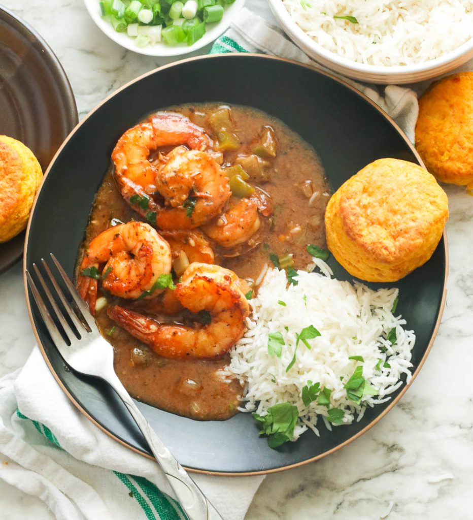 Shrimp gumbo served on a plate with cornbread muffin and rice