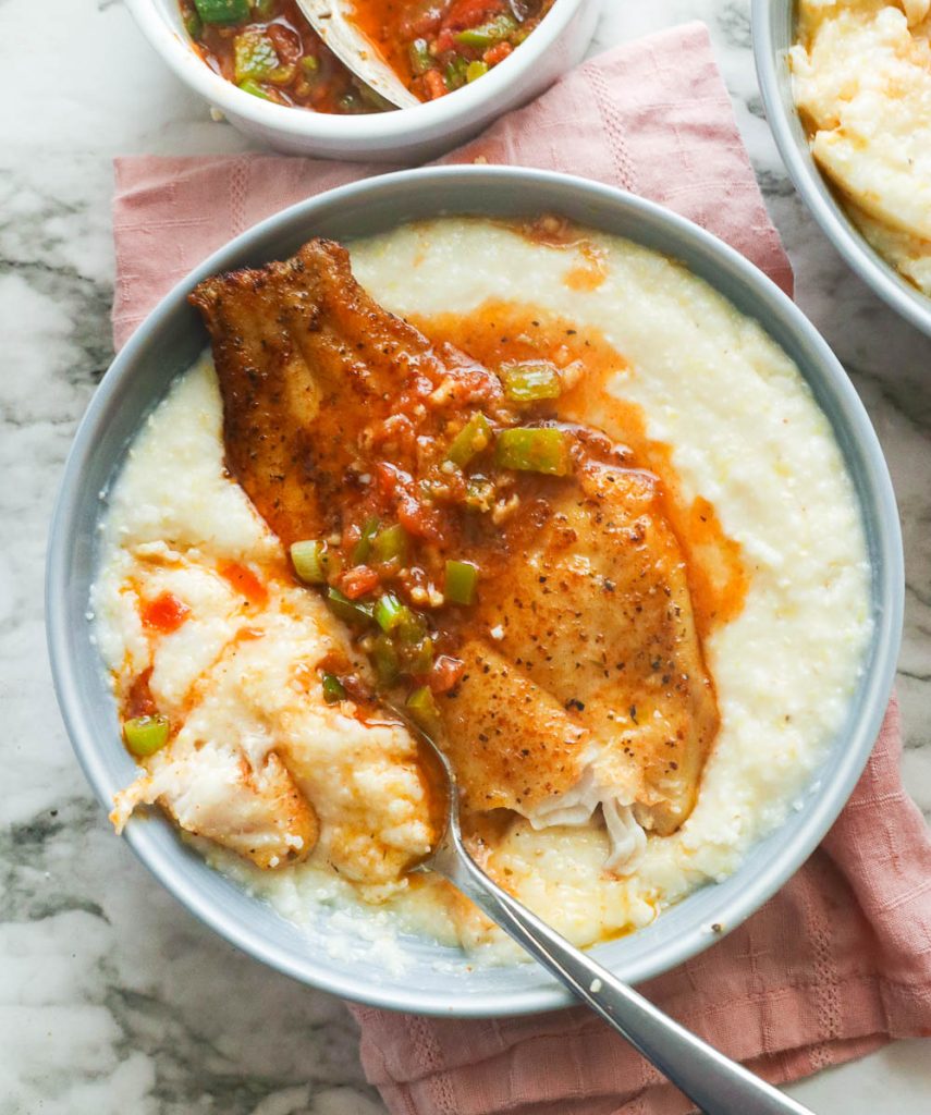 A bowl of grits with fried catfish smothered with sauce 