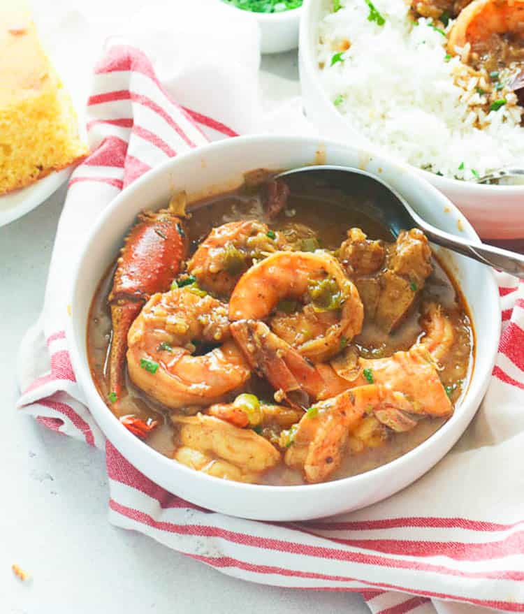 a bowl of shrimp gumbo with rice and cornbread in the background