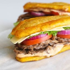 Two jibarito sandwiches with tomatoes, lettuce, onion, and steak.