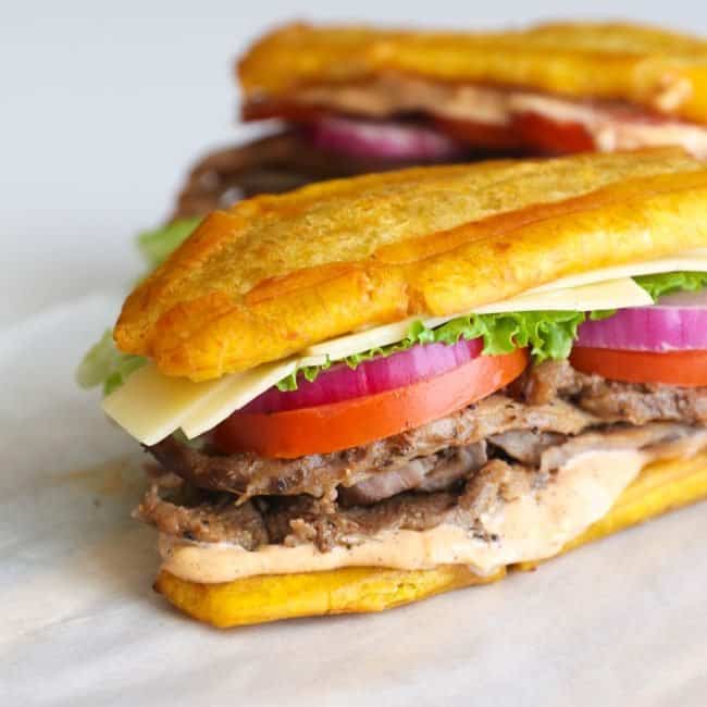 Two jibarito sandwiches with tomatoes, lettuce, onion, and steak.