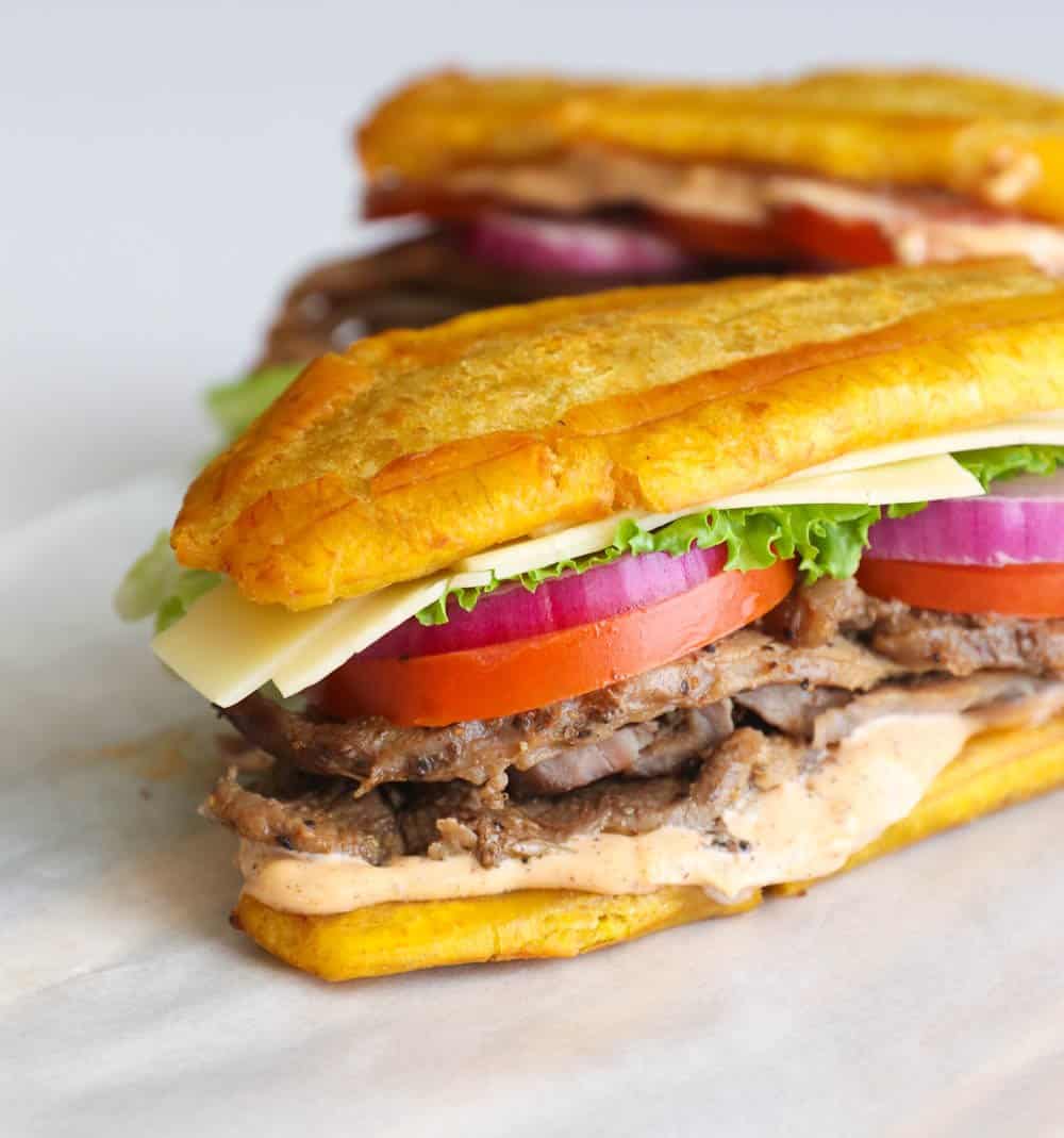 Two jibarito sandwiches with tomatoes, lettuce, onion, and steak.
