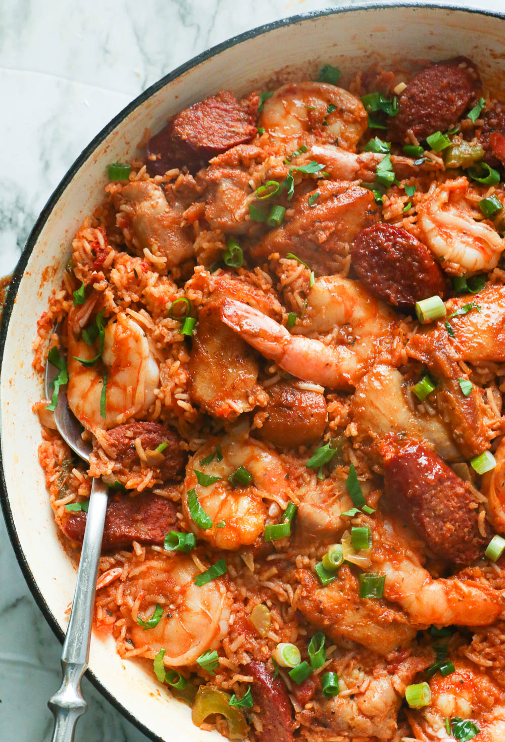 A pan of jambalaya garnished with green onions and a spoon ready to serve it with.