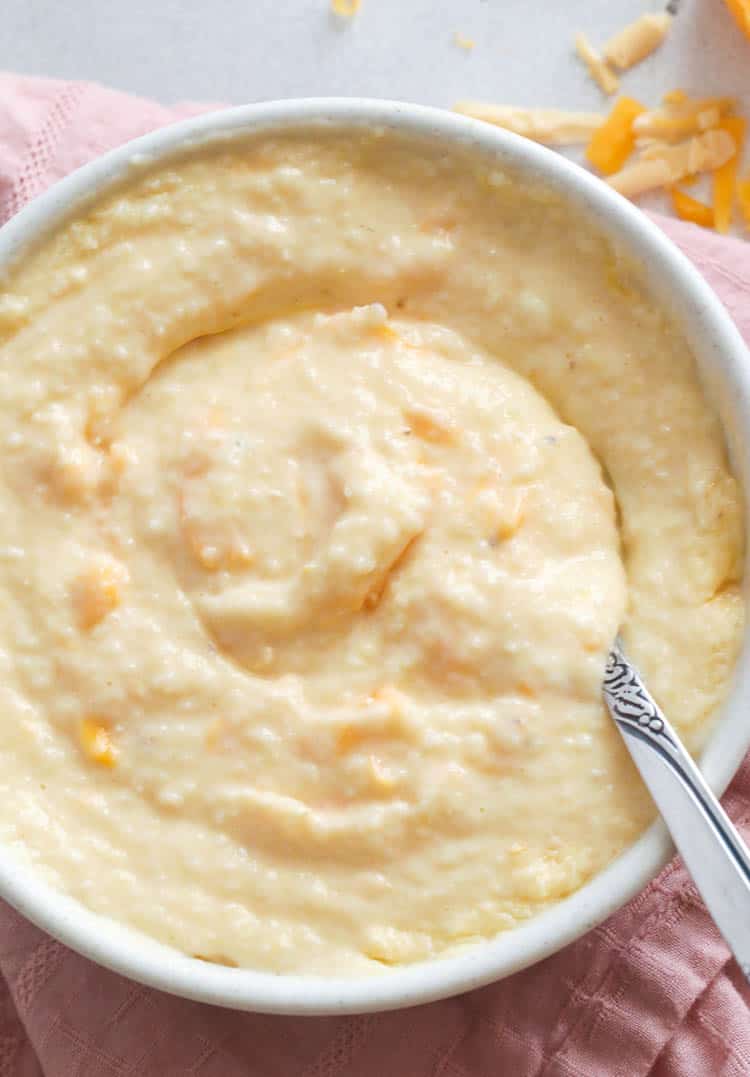 Stirring creamy cheesy grits in bowl with a spoon