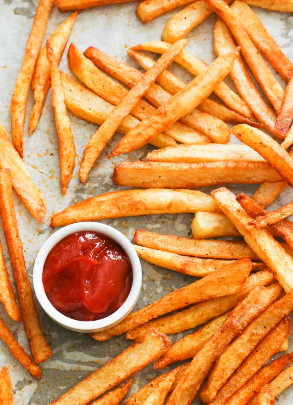 Seasoned fries with ketchup on a baking sheet.