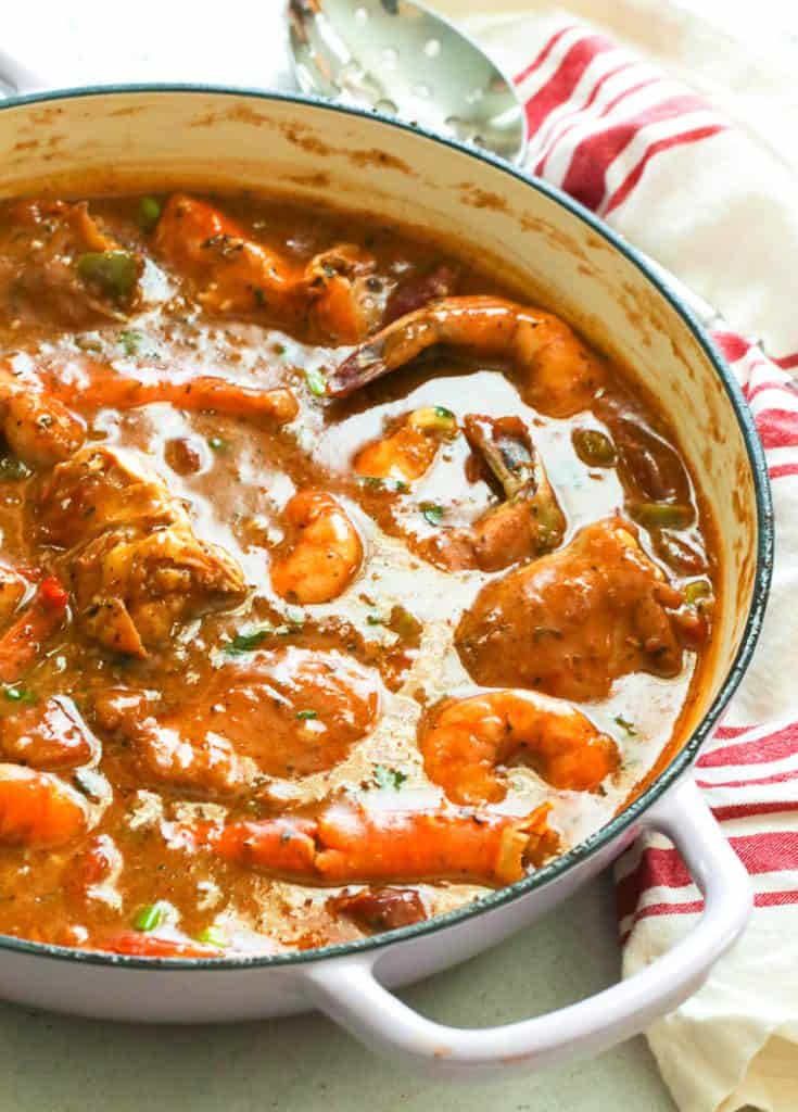 a pan of classic gumbo with a ladle and kitchen cloth in the background