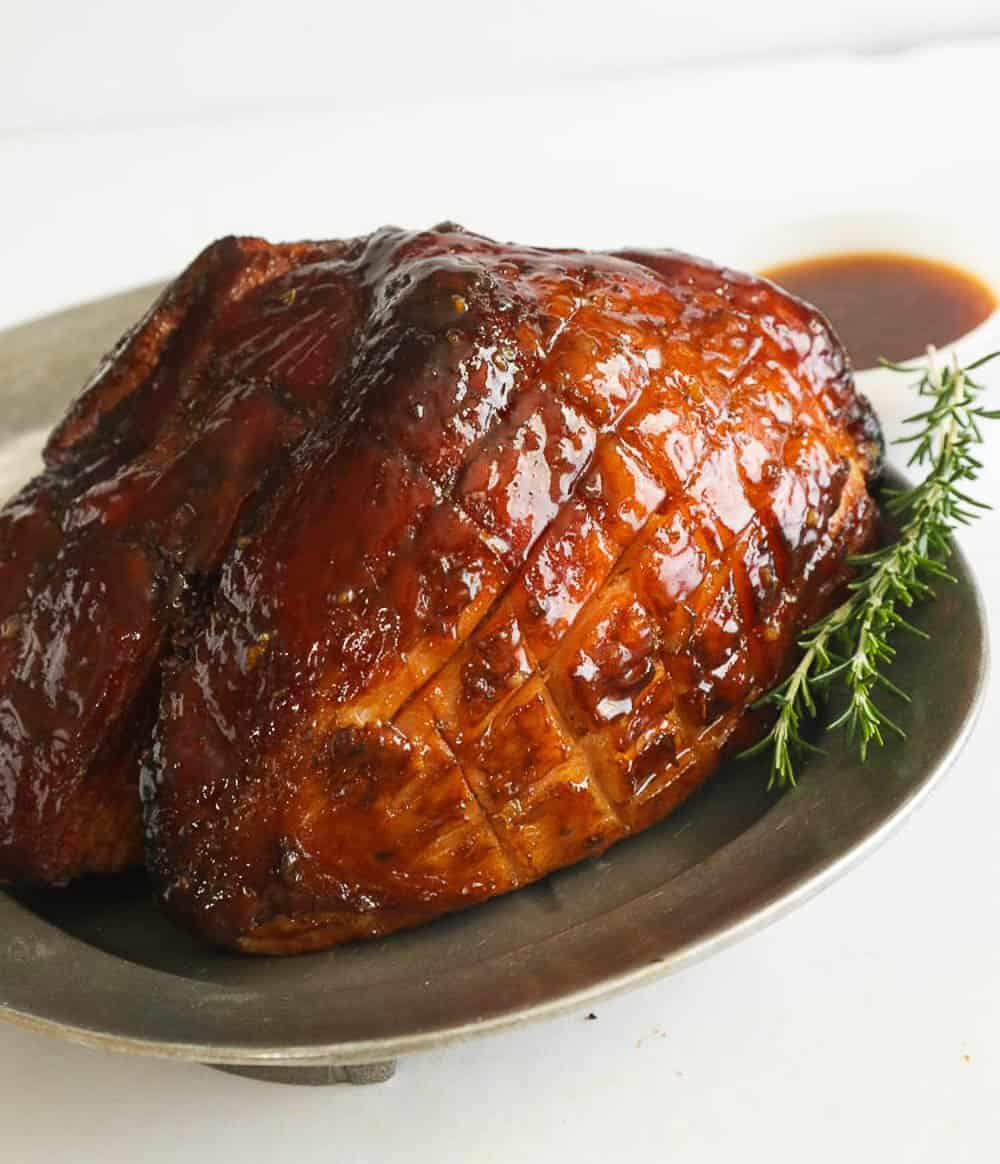 Whole smoked ham with extra glaze on the side and a sprig of rosemary