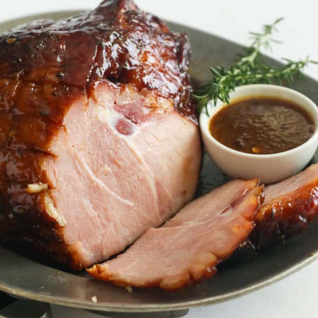 Smoked ham on a platter with a sprig of thyme and extra glaze