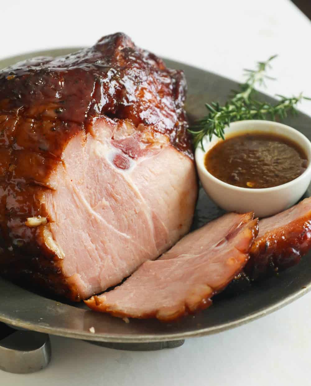 Smoked ham on a platter with a sprig of thyme and extra glaze