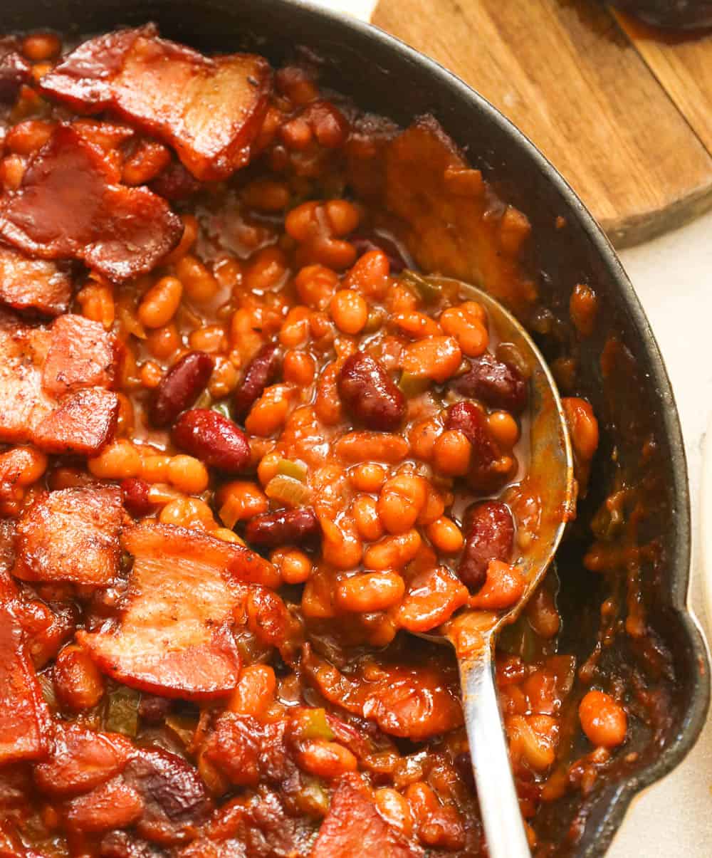 Southern Baked Beans with Bacon in a Skillet Being Spooned Out