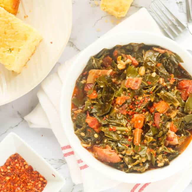 a bowl of southern collard greens served with cornbread with red pepper flakes in the background