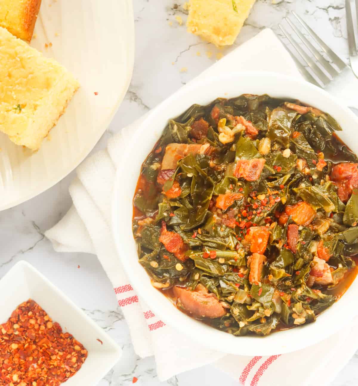 a bowl of southern collard greens served with cornbread with red pepper flakes in the background