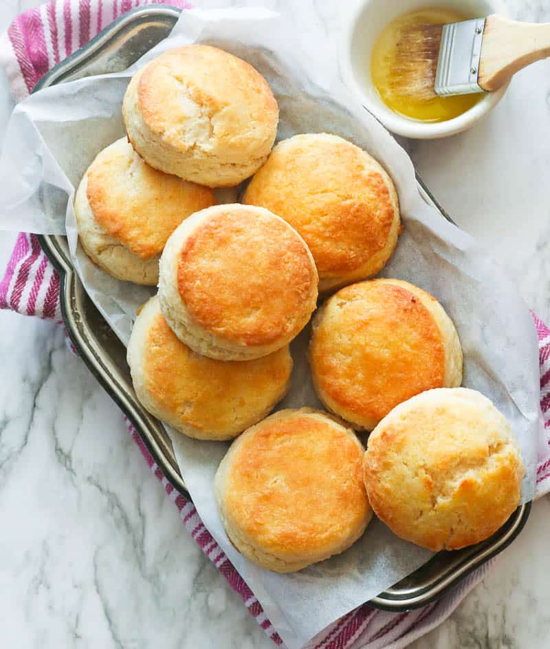Homemade buttermilk biscuits on a wax paper lined tray and butter on the side
