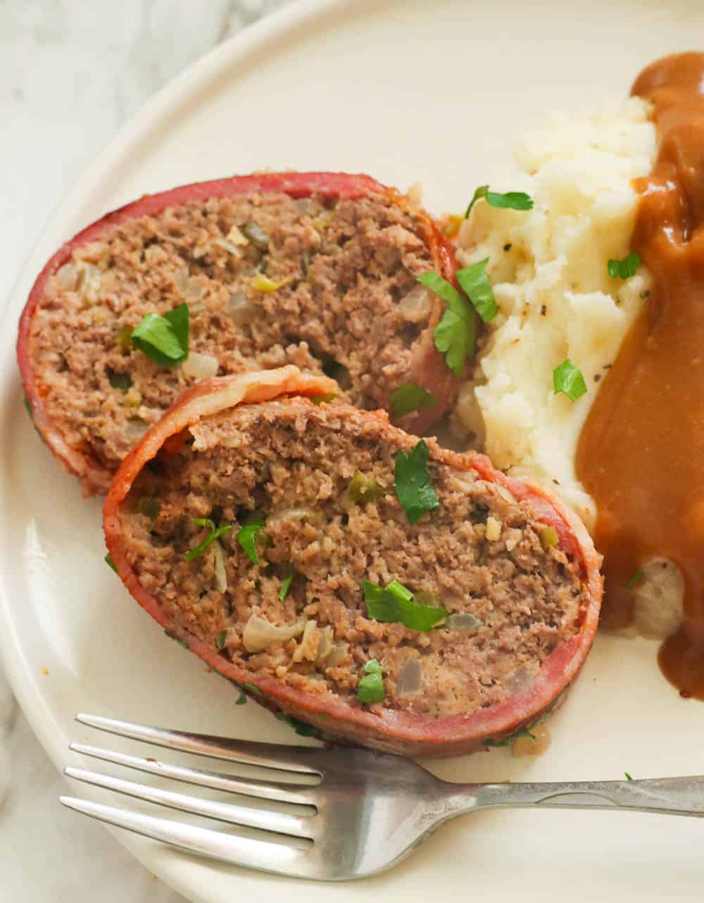 Sliced meatloaf with mashed potatoes, gravy, and parsley garnish