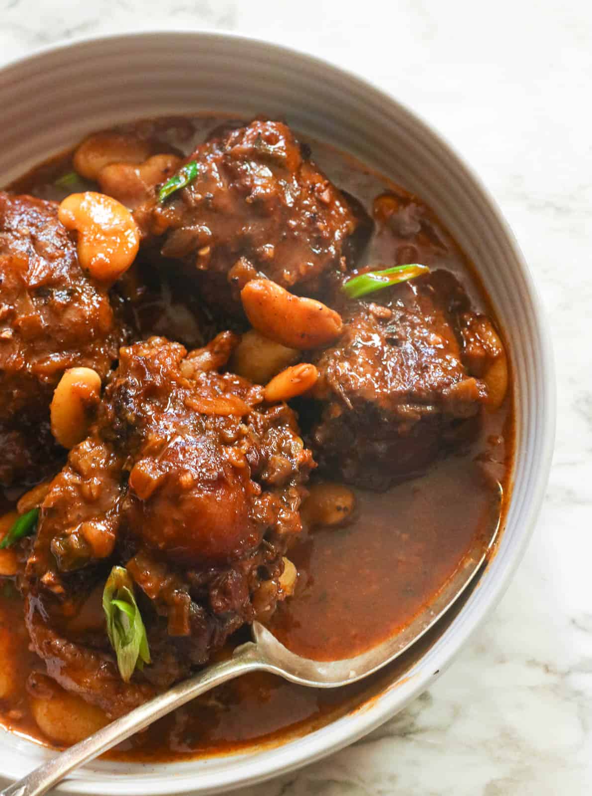 a close-up shot of Jamaican oxtail stew with beans in a white bowl