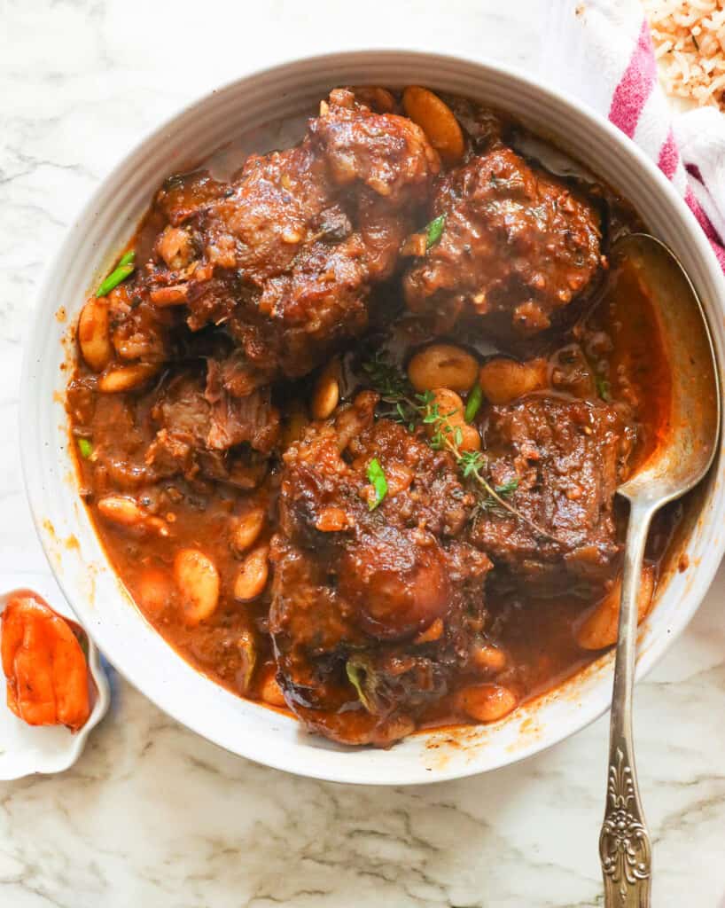 a bowl of Jamaican oxtail stew with a Scotch bonnet on the side