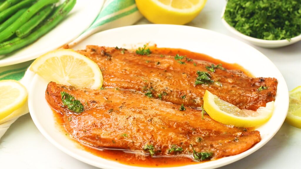 Two oven-baked tilapia fillets on a white plate