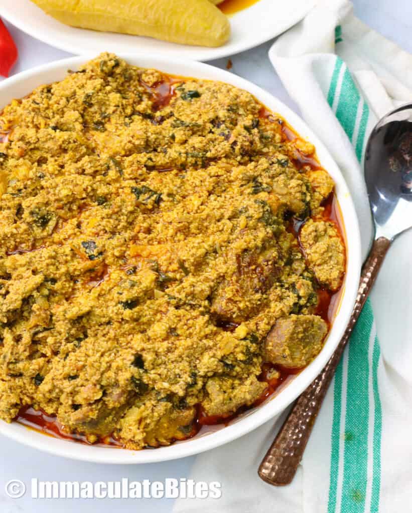 a bowl of egusi soup with plantains in the background