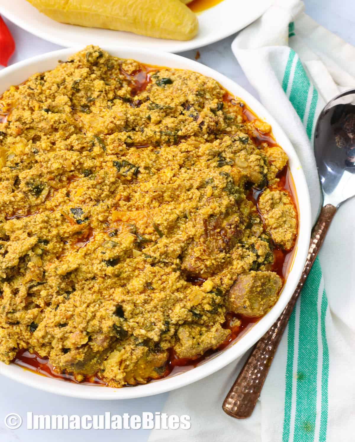a bowl of egusi soup with plantains in the background